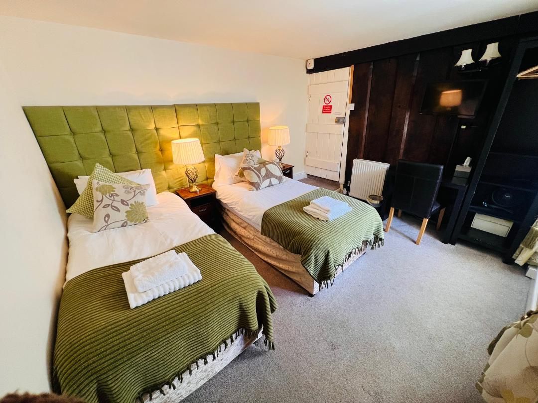 A hotel room with two beds, a chair, a desk, and a wardrobe.