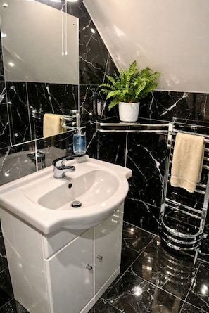 Un bagno con un lavandino bianco, uno specchio, una pianta su uno scaffale e un porta asciugamani.