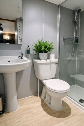A modern bathroom with a pedestal sink, toilet, and glass-enclosed shower.