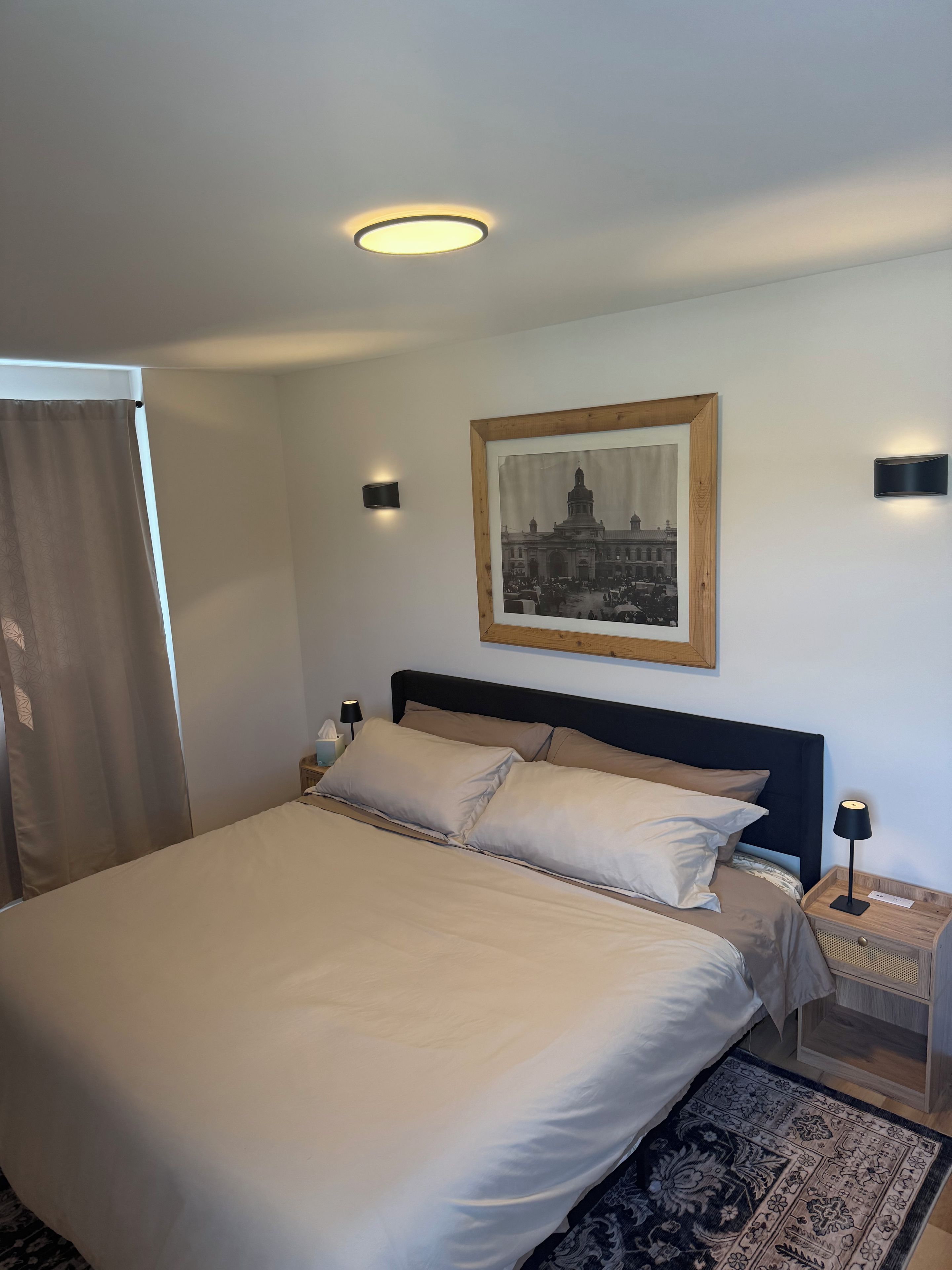 Habitación de hotel con una cama grande, un cuadro en la pared y una mesita de noche con una lámpara.