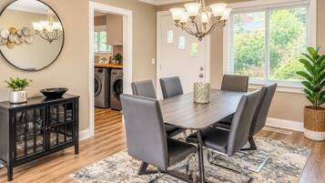 A dining area with a dark wood table, grey upholstered chairs, a chandelier, and a view of a laundry room through an open door.