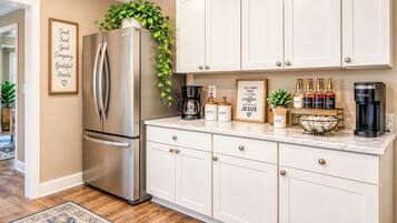 A modern kitchen with white cabinetry, a stainless steel refrigerator, a coffee maker, and a Keurig coffee maker.