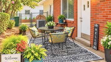 A patio with a table and chairs, surrounded by potted plants and a welcome mat.