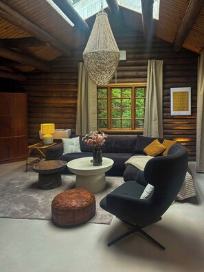 A cozy log cabin interior with a large window, a hanging light fixture, a sofa, a coffee table, and a chair. - Timber-framed house with sedum roof in nature (Frederiksværk)