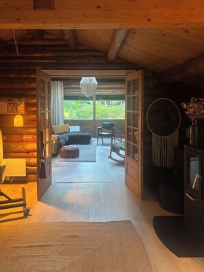 Interior de cabana de tronco com cama, área de estar e vista para o verde lá fora.