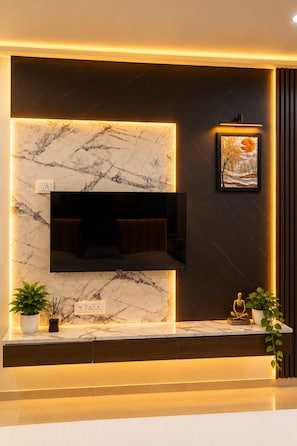 Una sala de estar moderna con una pared de mármol, un televisor montado y una obra de arte enmarcada.