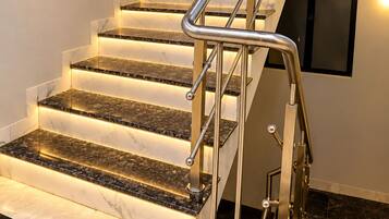 Una escalera con barandilla de metal, escalones de mármol e iluminación empotrada en la pared.