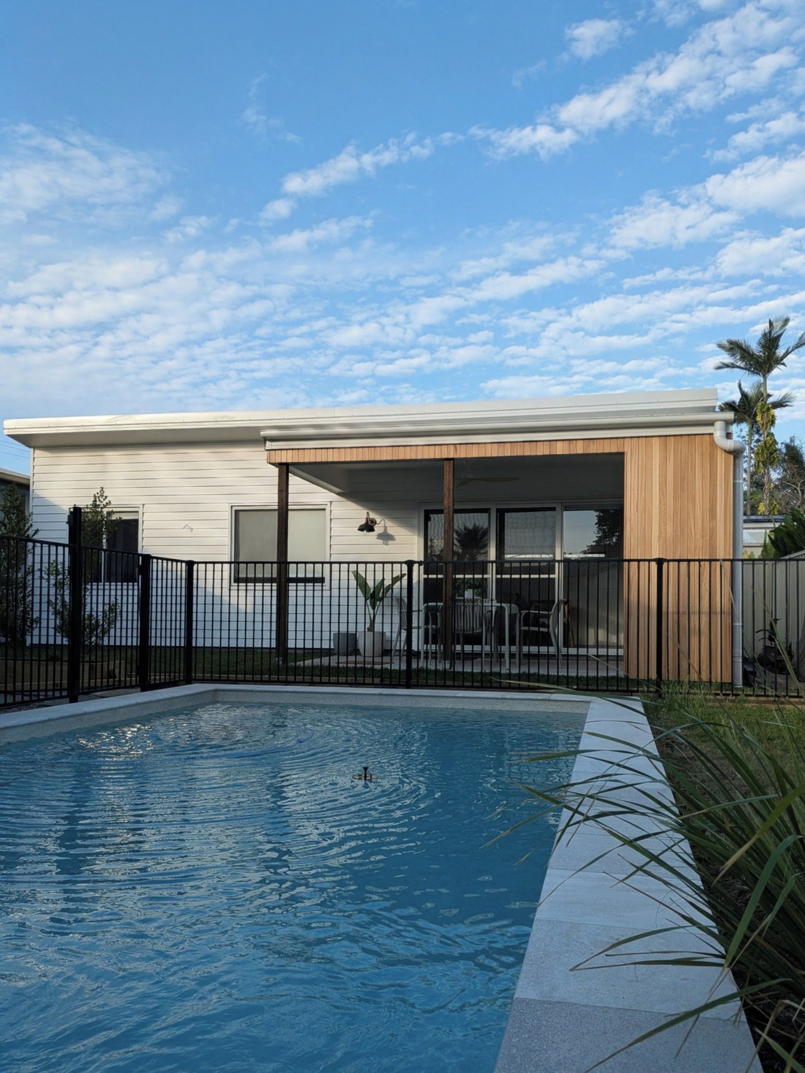 Une maison moderne avec une piscine, un patio clôturé et un ciel d’un bleu éclatant.
