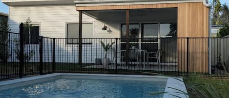 Et moderne hus med swimmingpool, en indhegnet terrasse og en klar blå himmel.