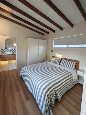 Ein Schlafzimmer mit einem Bett, Holzbalken, einem Fenster, einem Nachttisch und einem Kleiderschrank.