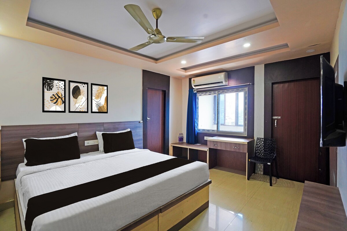 A hotel room with a bed, a desk, a chair, a ceiling fan, and artwork on the wall.