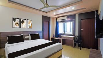 A hotel room with a bed, a desk, a chair, a ceiling fan, and artwork on the wall.