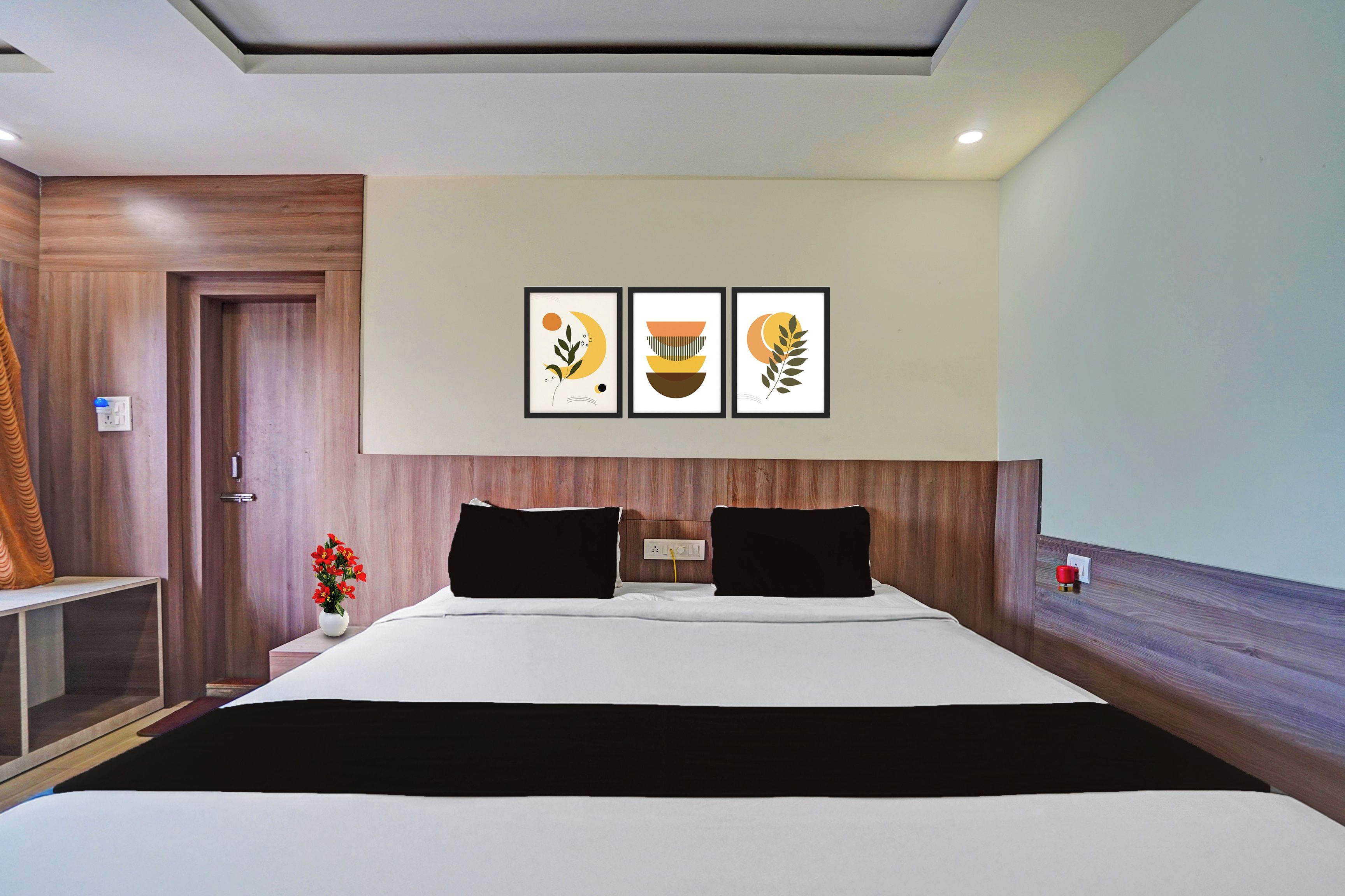 A hotel room with a bed, a nightstand, a vase with flowers, and three framed wall art pieces.