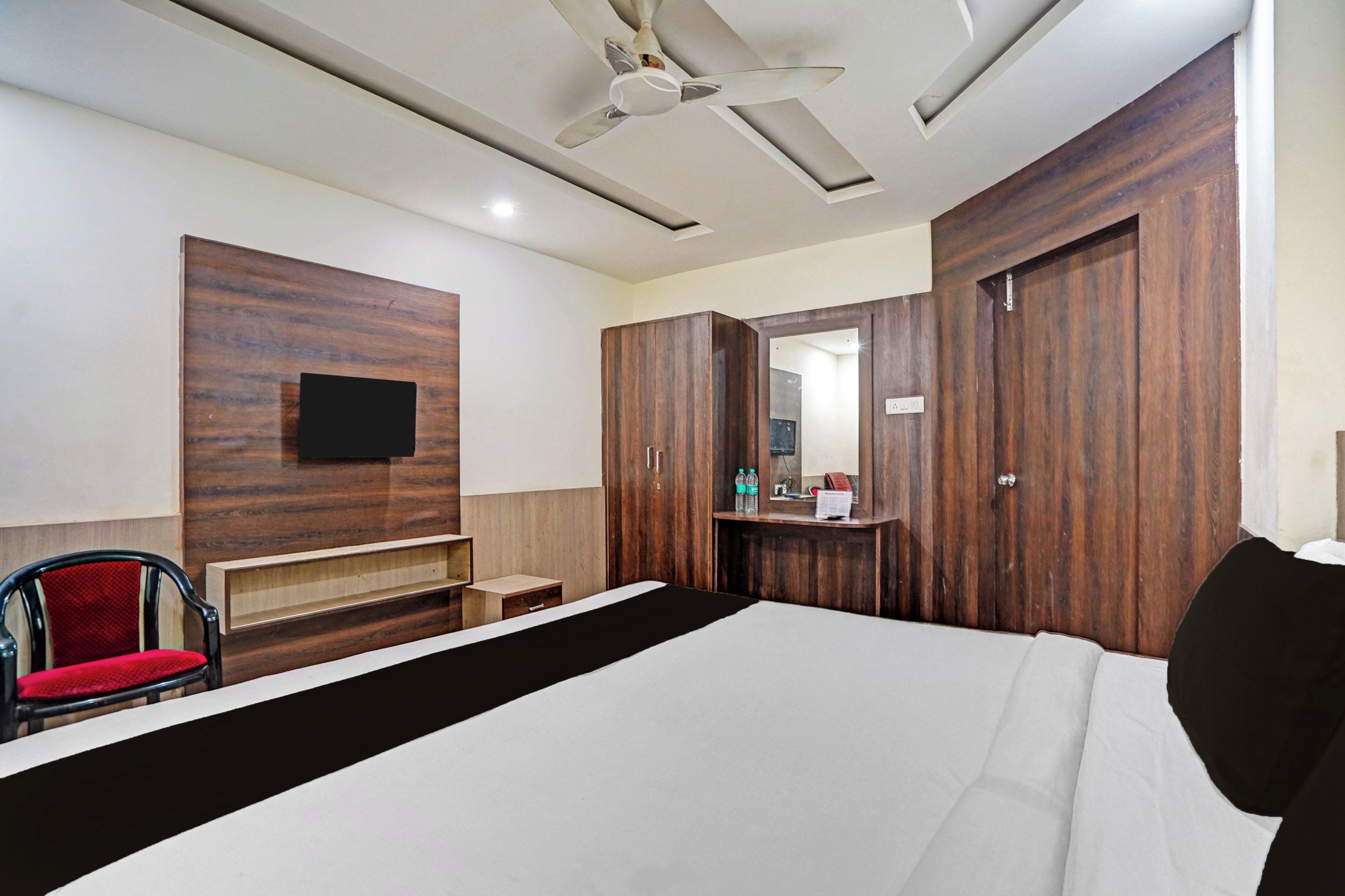 A hotel room with a bed, a desk, a chair, a mirror, and a ceiling fan.