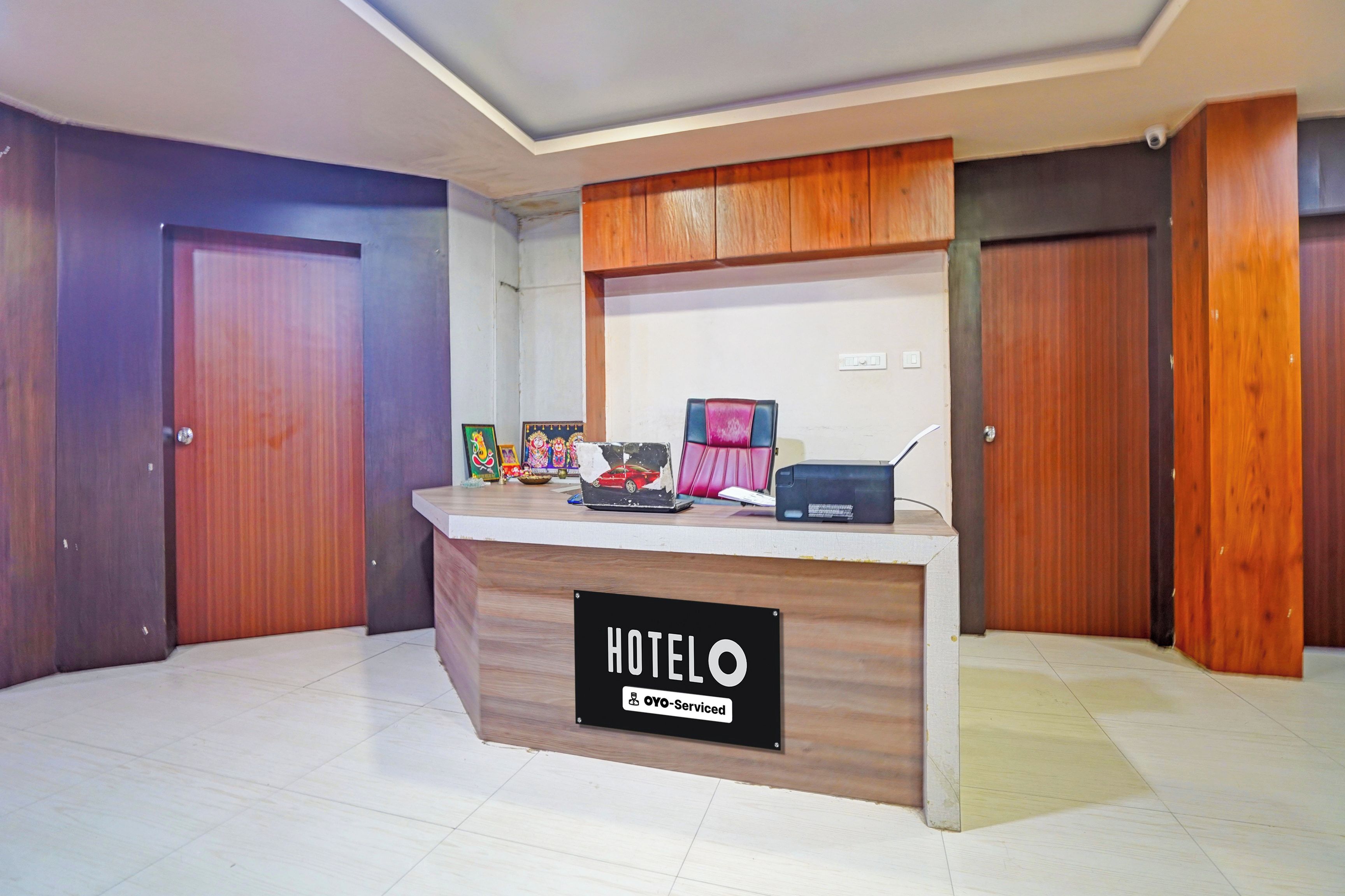 A reception desk with a sign reading 'HOTELO OYO-Serviced' in a hotel lobby with wooden doors and a tiled floor.