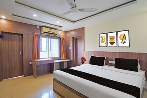 A hotel room with a bed, a desk, a window with curtains, an air conditioning unit, and wall art. - Hotel O Kalinga Stadium Formerly Anusuya (Bhubaneshwar)