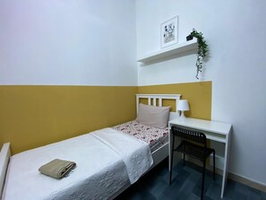 A single bed with a white headboard, a bedside table with a lamp, and a chair.