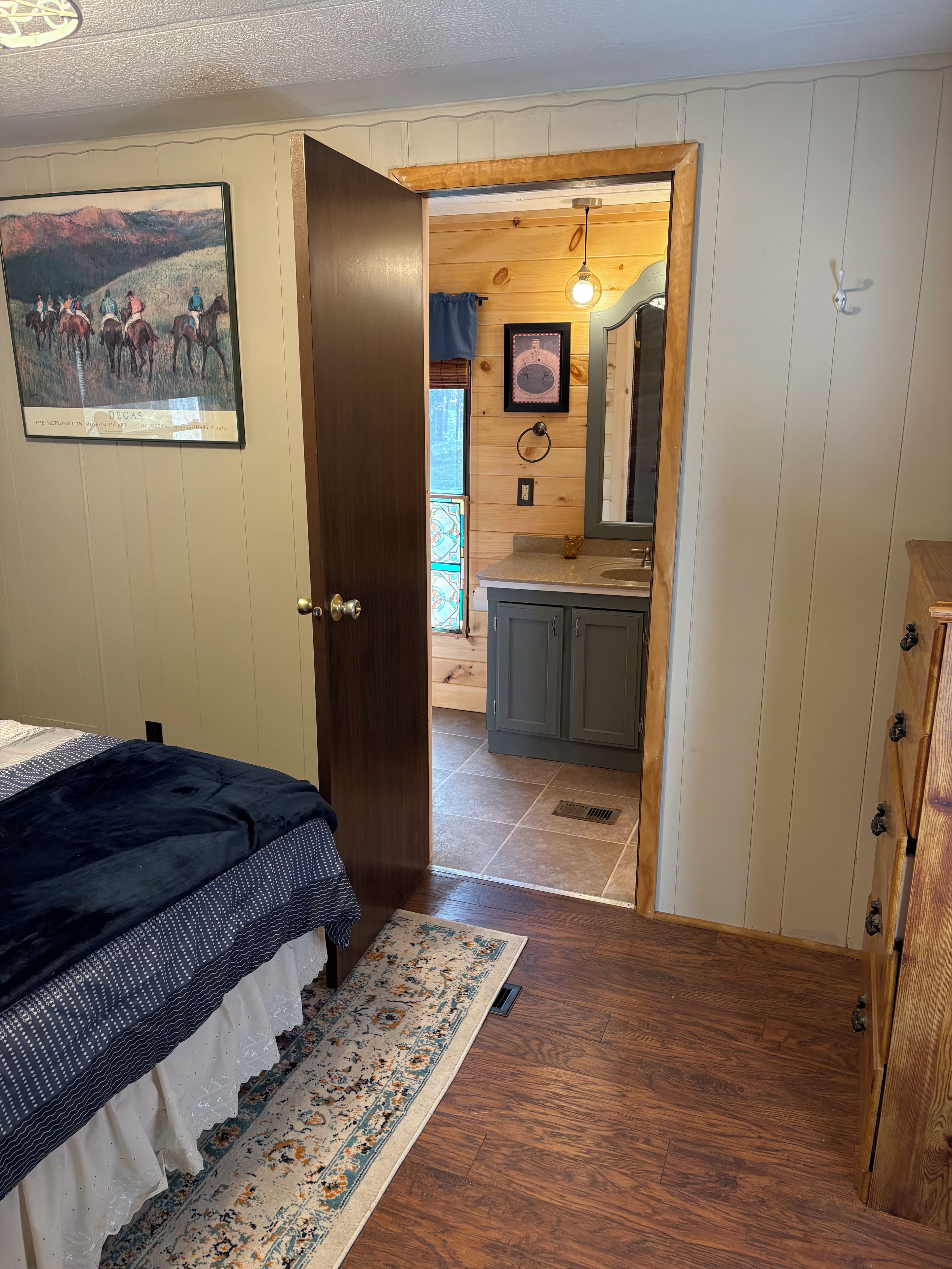 A bedroom with a bed, a rug, a wooden door leading to a bathroom with a sink and mirror.