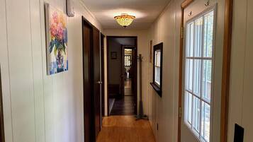 A hallway with wooden flooring, a ceiling light fixture, and a door with a window.