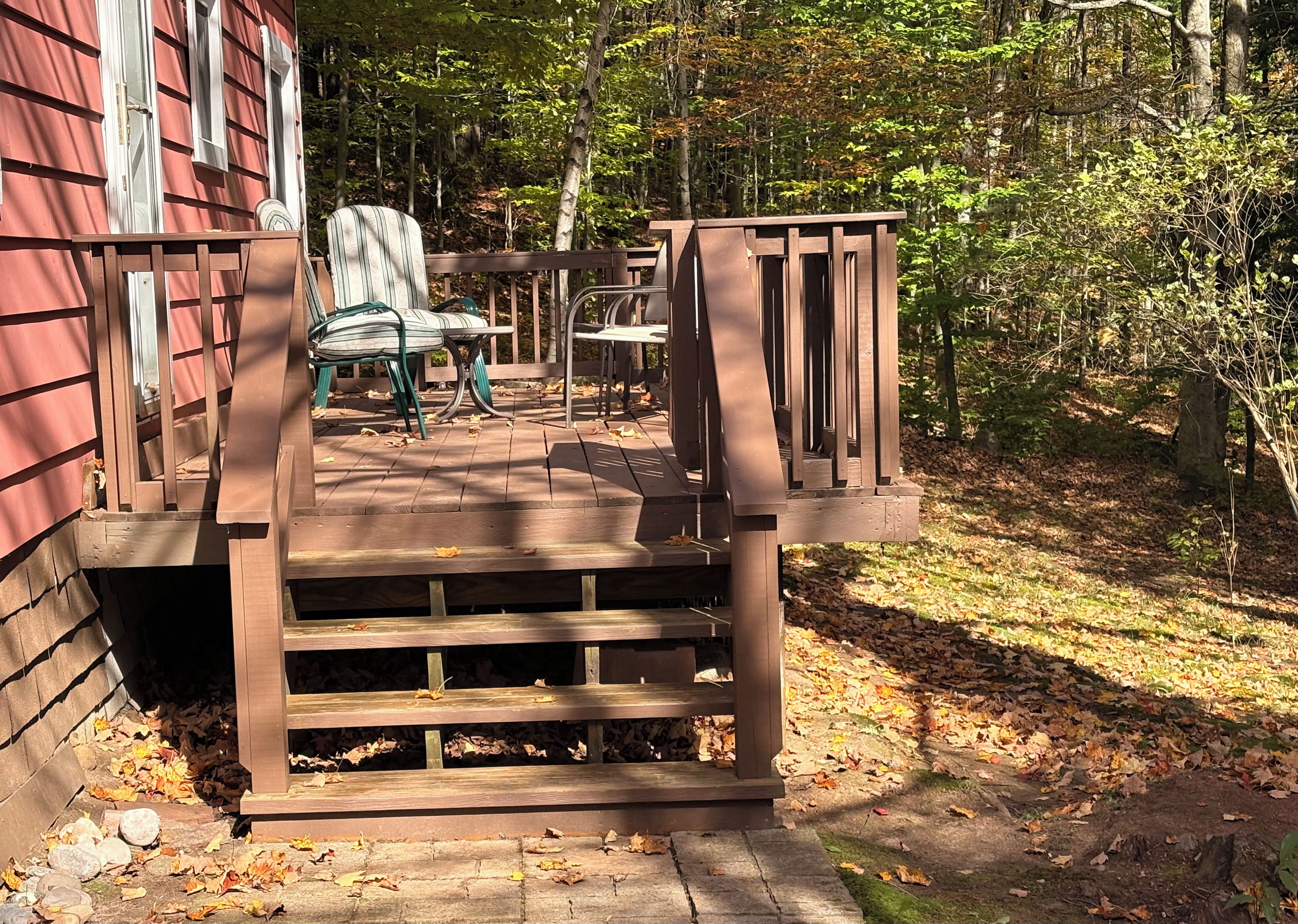 A wooden deck with a staircase leading to a covered area with outdoor furniture.