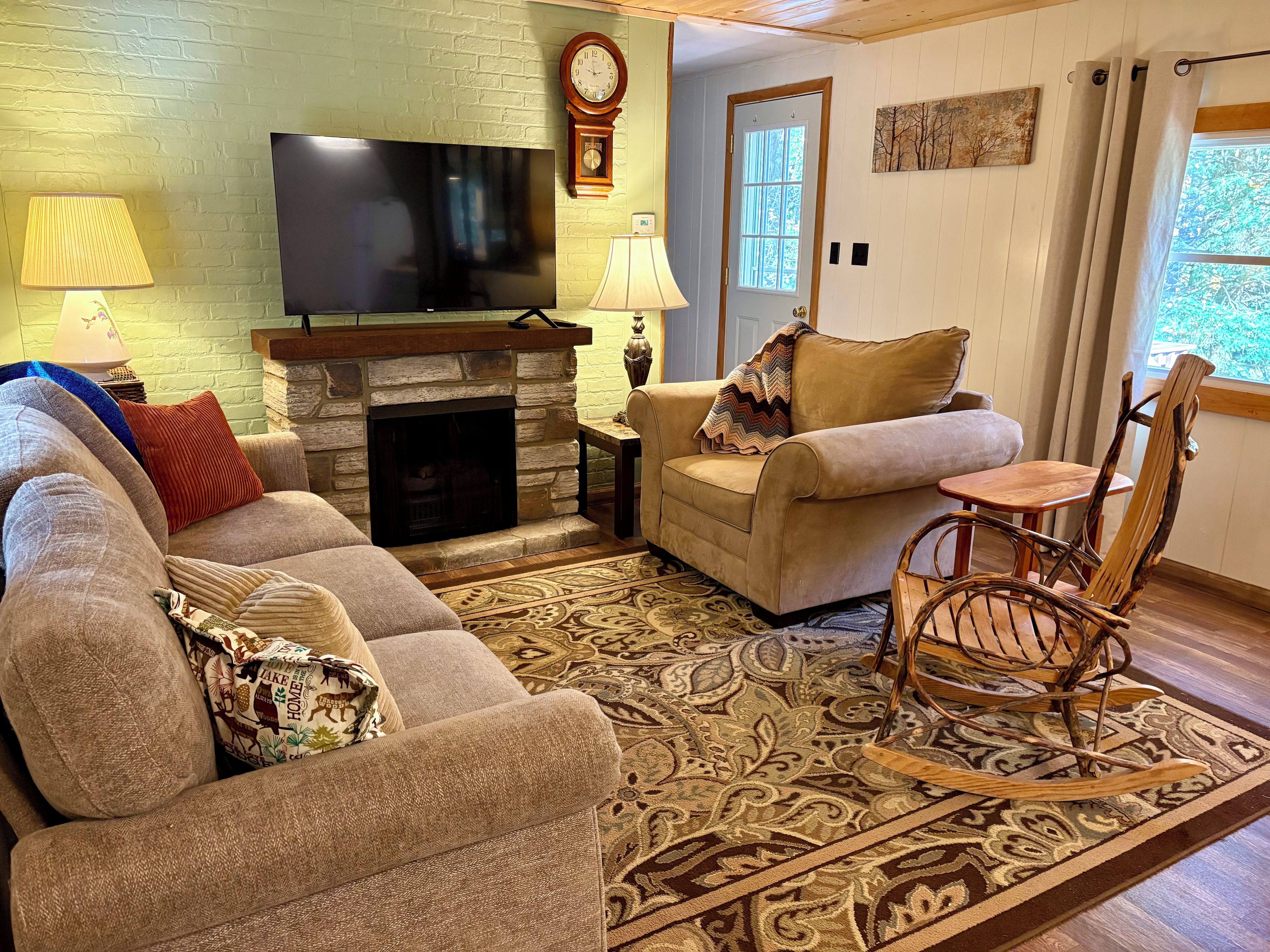 A living room with a stone fireplace, a television, and a rocking chair.