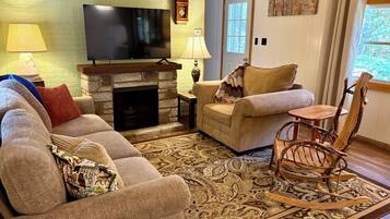 A living room with a stone fireplace, a television, and a rocking chair.