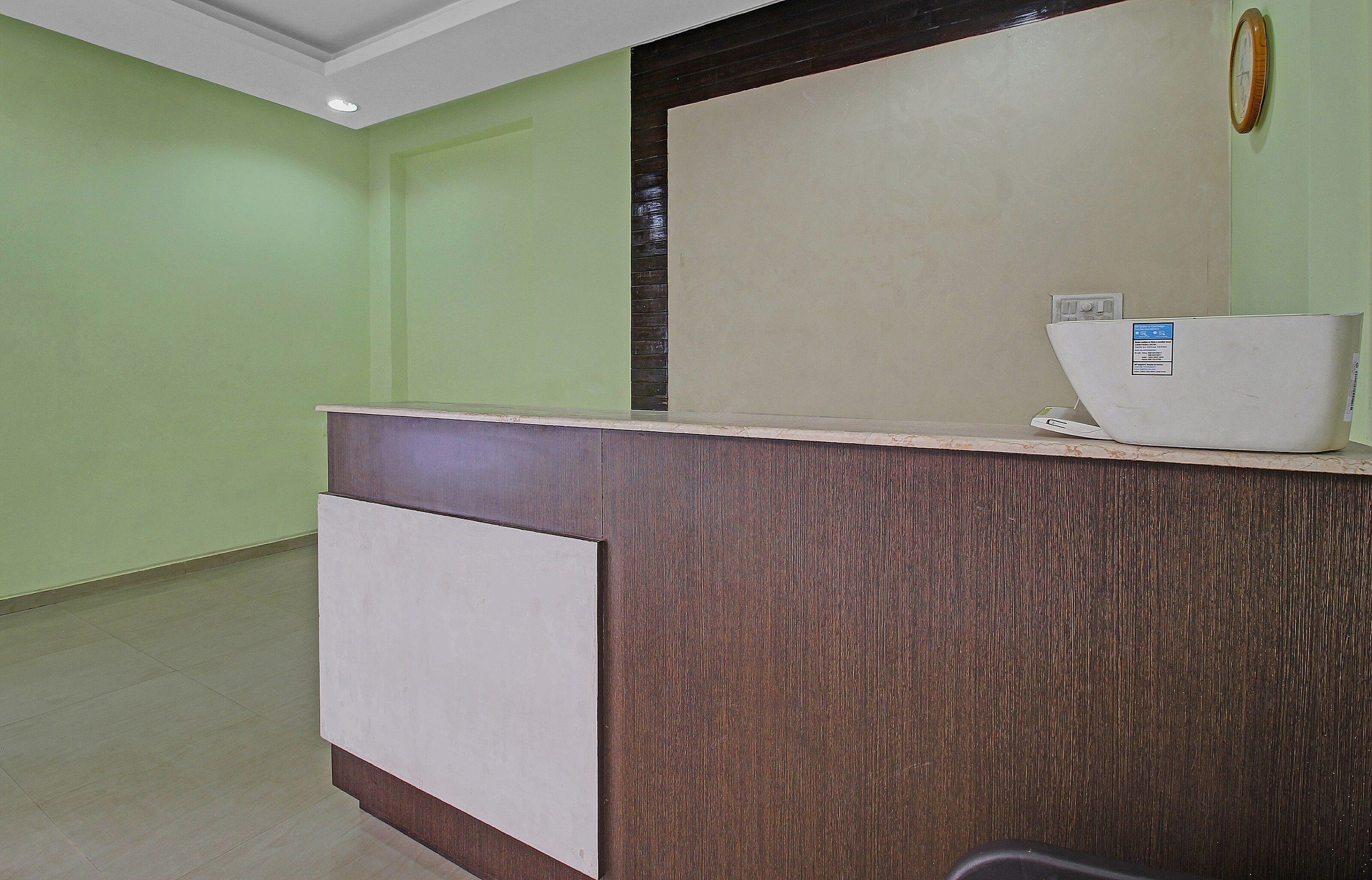 Un mostrador de recepción con detalles de madera y un panel blanco, un reloj en la pared y un pequeño dispositivo electrónico sobre el mostrador.