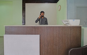 En receptionsdisk med en klocka på väggen, en dator på disken och ett fönster med persienner.