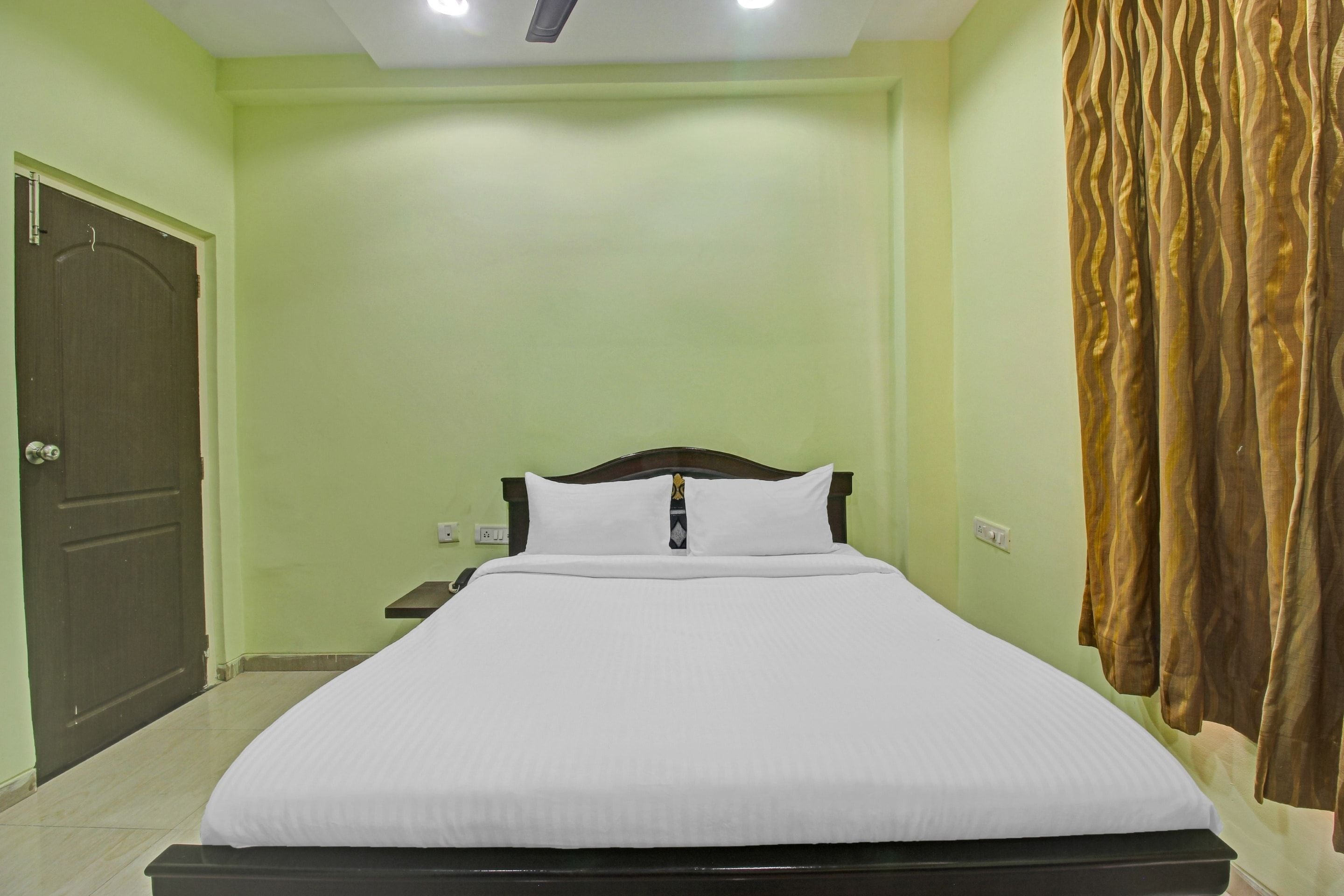 Una cama bien hecha en una habitación con pared verde, puerta de madera y cortina.