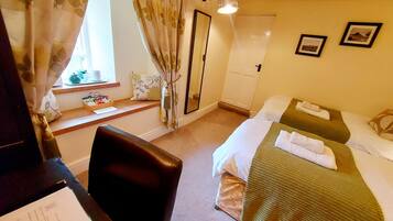 A hotel room with a desk, two beds, a mirror, and a window with curtains.