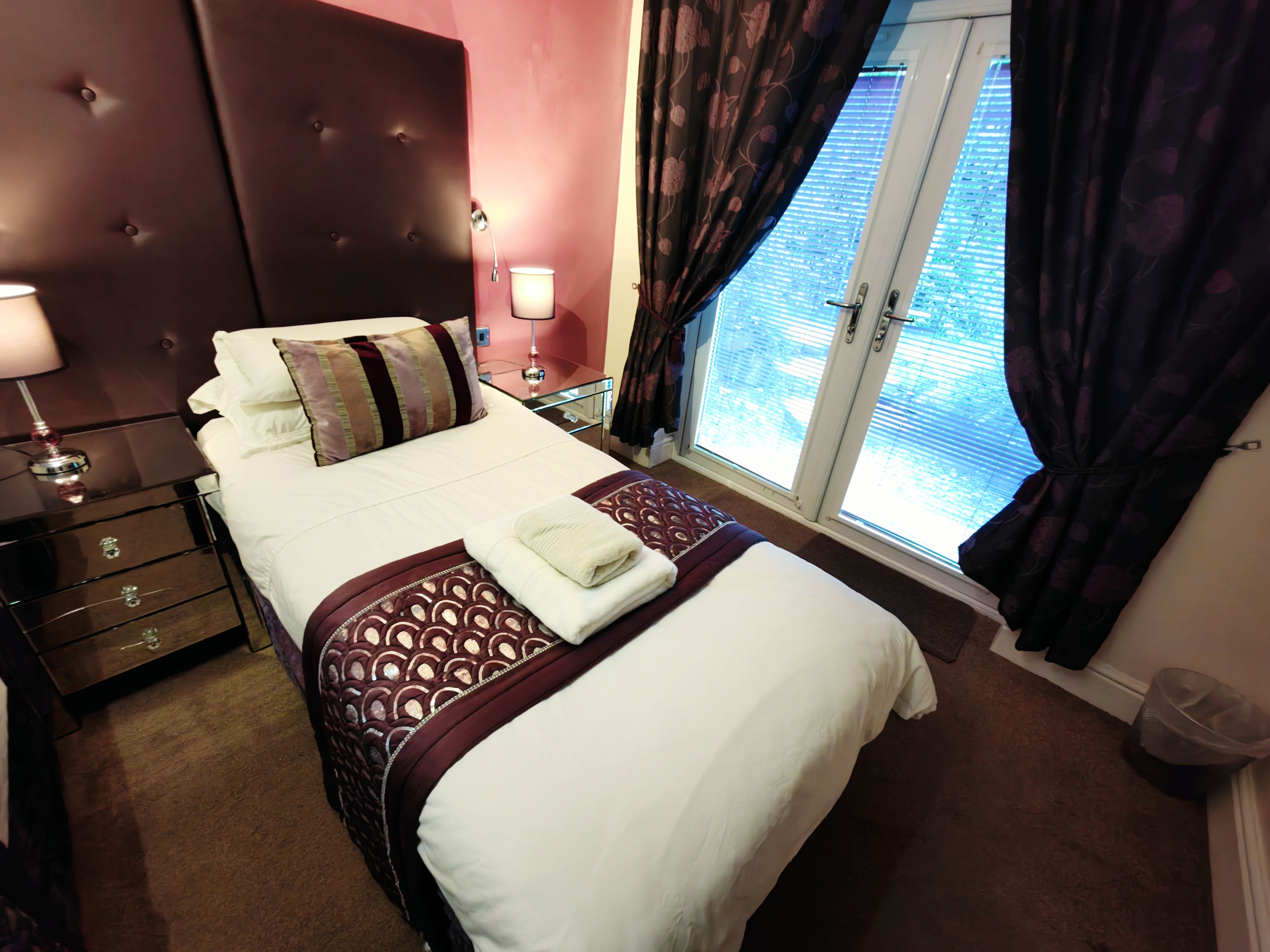 A hotel room with a large bed, bedside tables, a nightstand, a window with curtains, and a view of the outside.