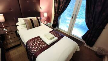 A hotel room with a large bed, bedside tables, a nightstand, a window with curtains, and a view of the outside.