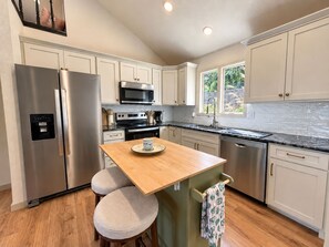 A modern kitchen with stainless steel appliances, a wooden island, and a view of greenery outside. - The Sunny Perch - Lakefront Home (Osage Beach)