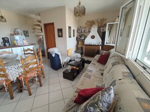 A living room with a sofa, a dining table with chairs, a fireplace, and a chandelier. - Tranquil 2-Bed Village Haven in Episkepsi - Ideal Long-Stay Retreat (Episkepsi)