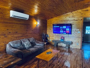 A cozy room with a leather sofa, a wooden coffee table, and a flat-screen TV mounted on the wall displaying a streaming service interface.