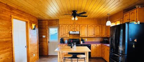 A wooden-paneled kitchen with a central island, a black refrigerator, and wooden cabinets.