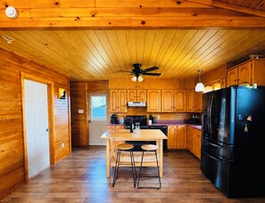A wooden-paneled kitchen with a central island, a black refrigerator, and wooden cabinets.