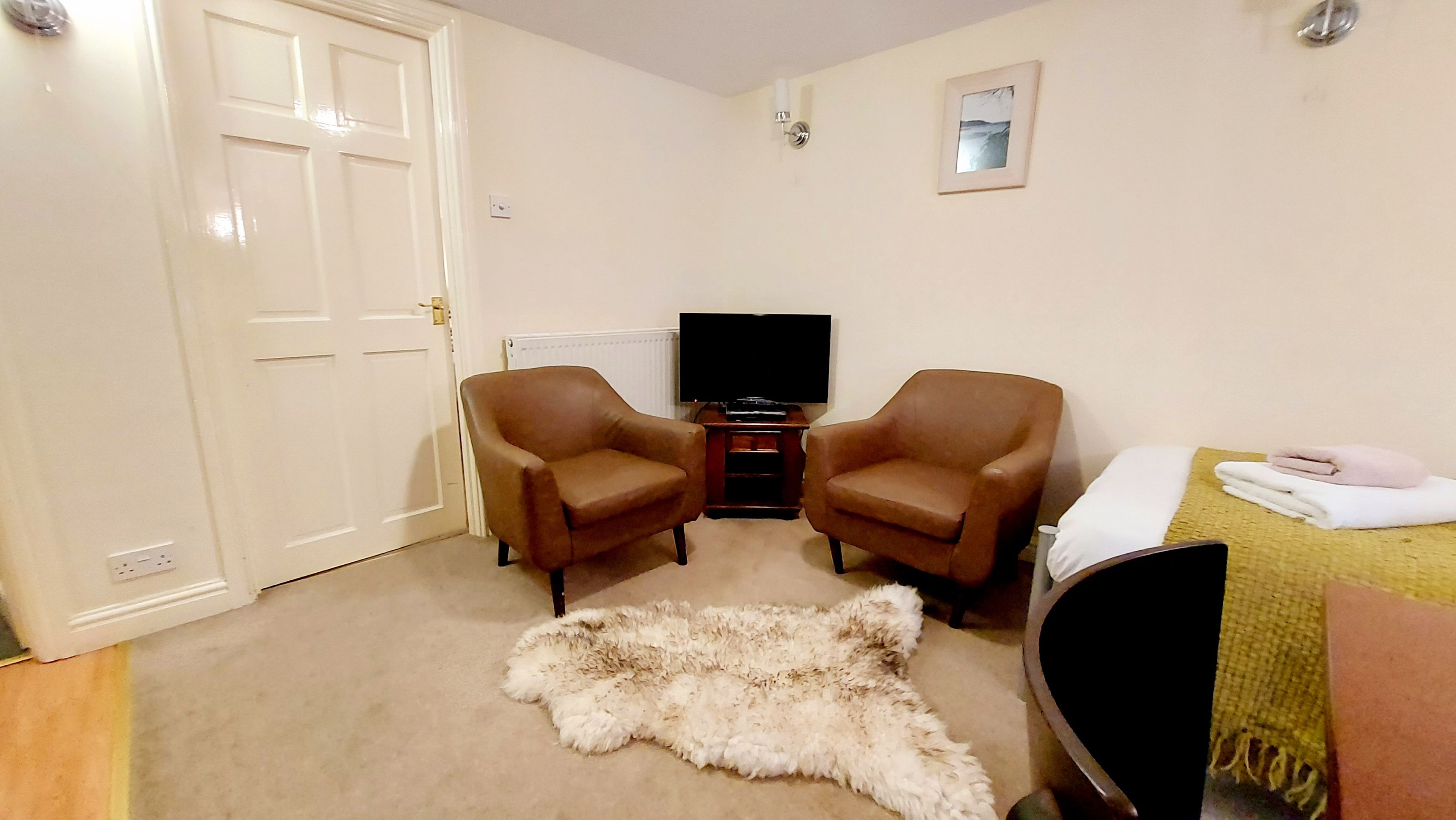 A room with two brown leather chairs, a television on a stand, a fur rug, and a bed with a yellow blanket.