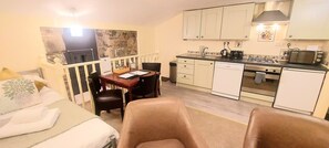 Camera d'albergo compatta con letto, un piccolo tavolo da pranzo, angolo cottura e balcone con parete in pietra.
