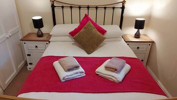 A neatly made bed with a red blanket, two pillows, and two folded towels.