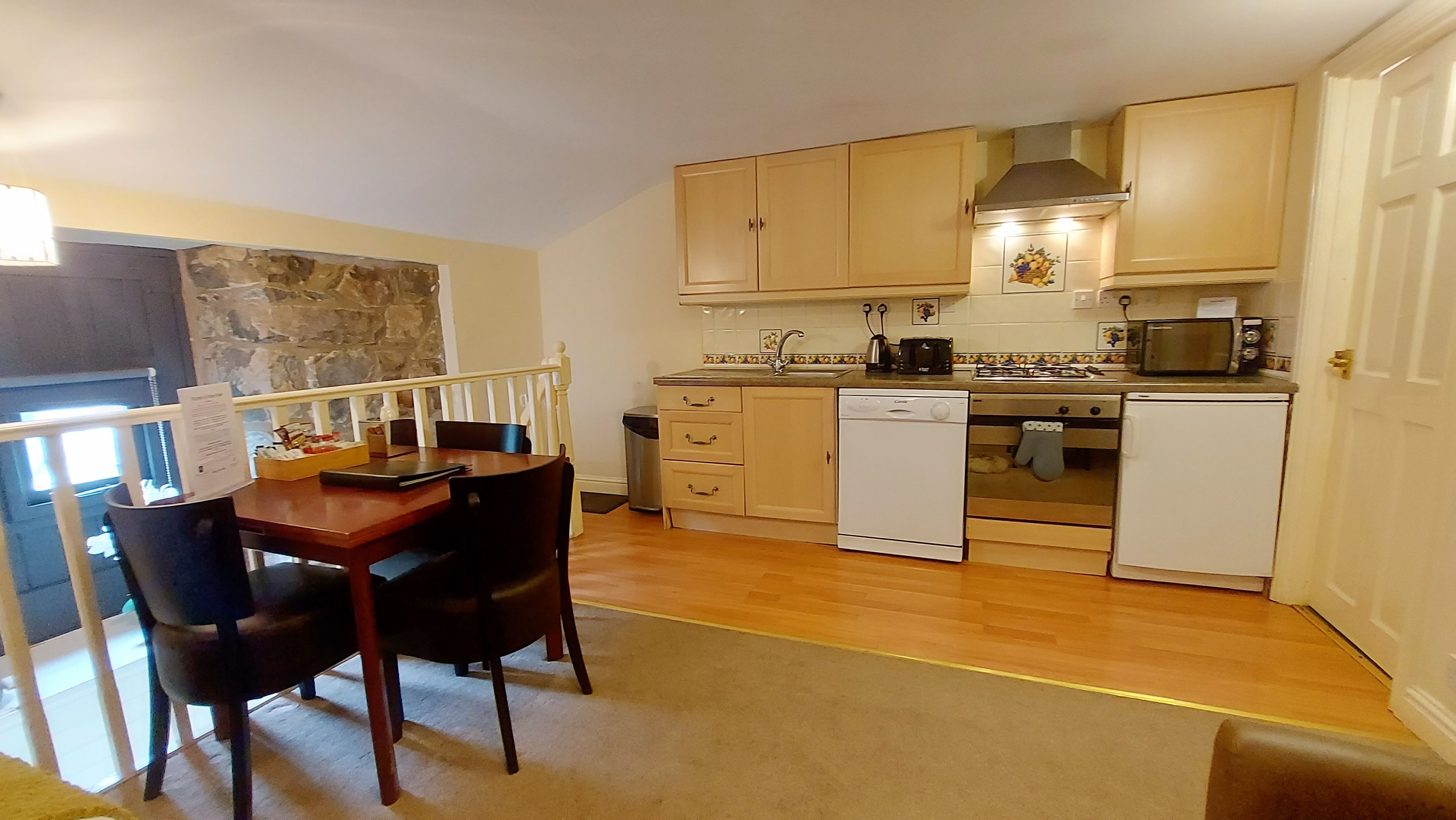 A compact kitchen with wooden cabinets, a dishwasher, a microwave, and a dining area with a table and chairs.