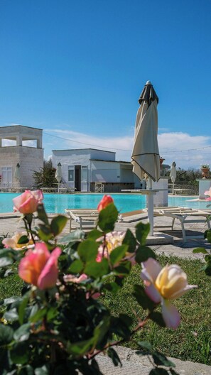 A swimming pool with lounge chairs and umbrellas, surrounded by buildings and greenery. - Villa close to the beach in Torre dell'Orso (Melendugno)