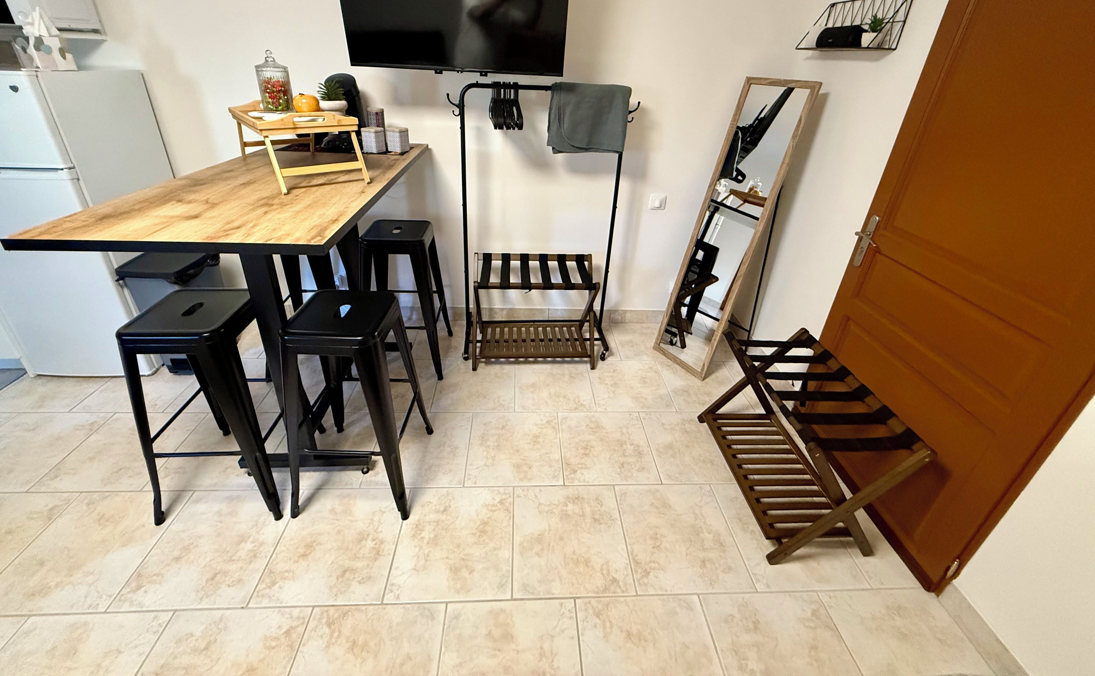 Una cucina compatta con un tavolo di legno, sgabelli neri e una rastrelliera, oltre a uno specchio.