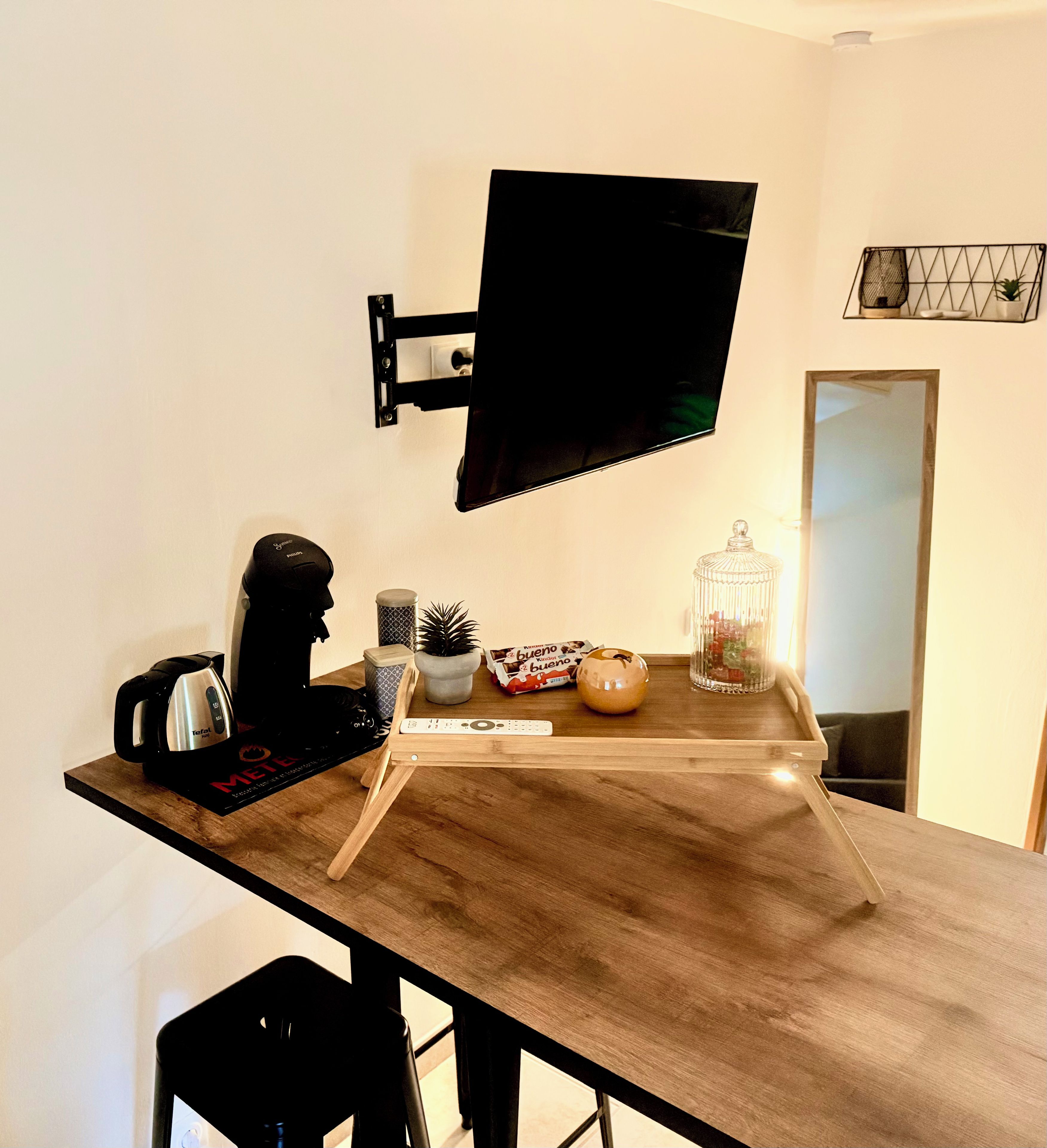 A modern kitchen with a wooden countertop, a mounted television, a kettle, a remote control, and decorative items.