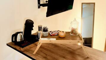 A modern kitchen with a wooden countertop, a mounted television, a kettle, a remote control, and decorative items.