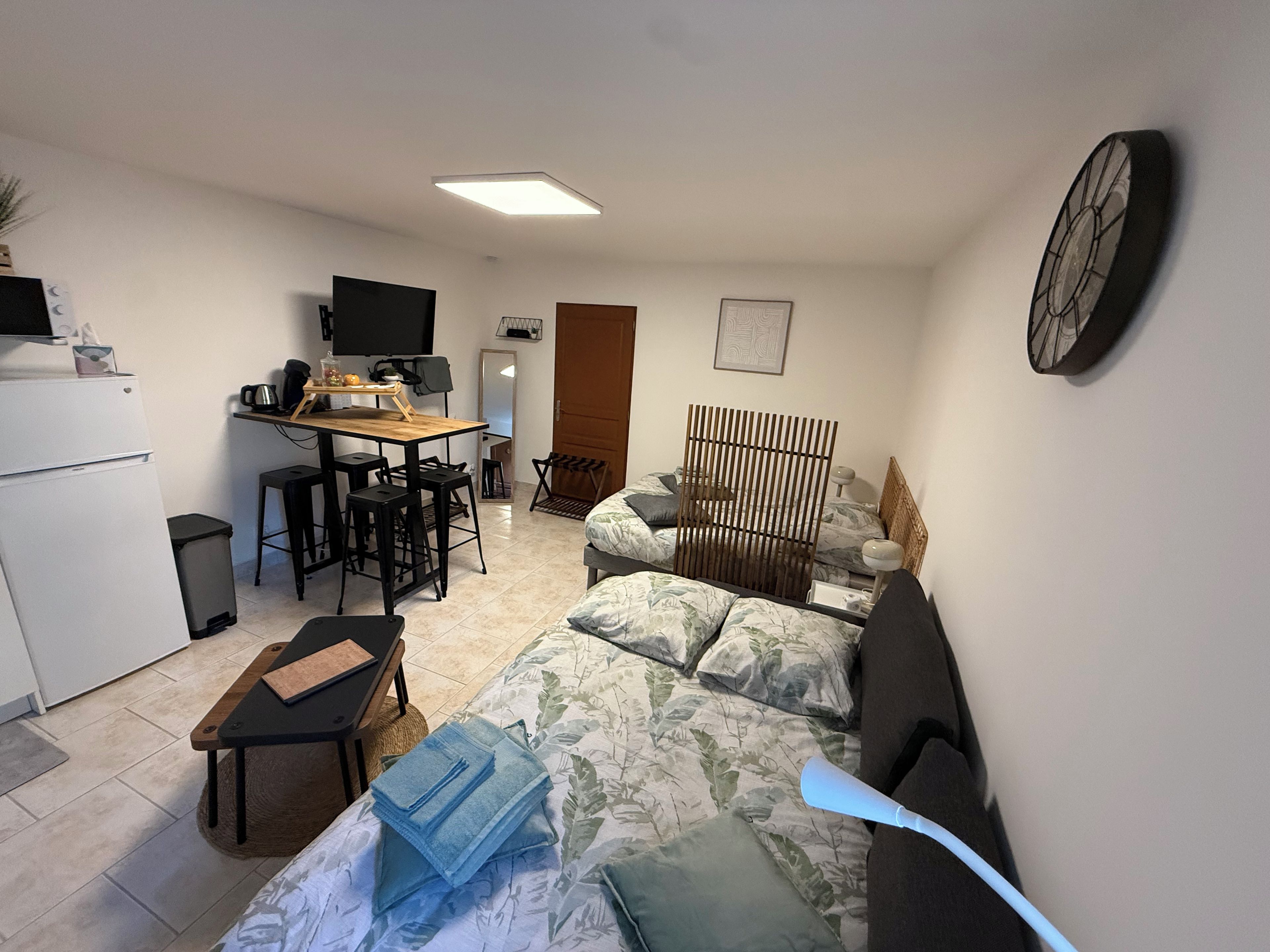 A compact living space with a kitchenette, a bed with floral bedding, a desk with a chair, and a television.