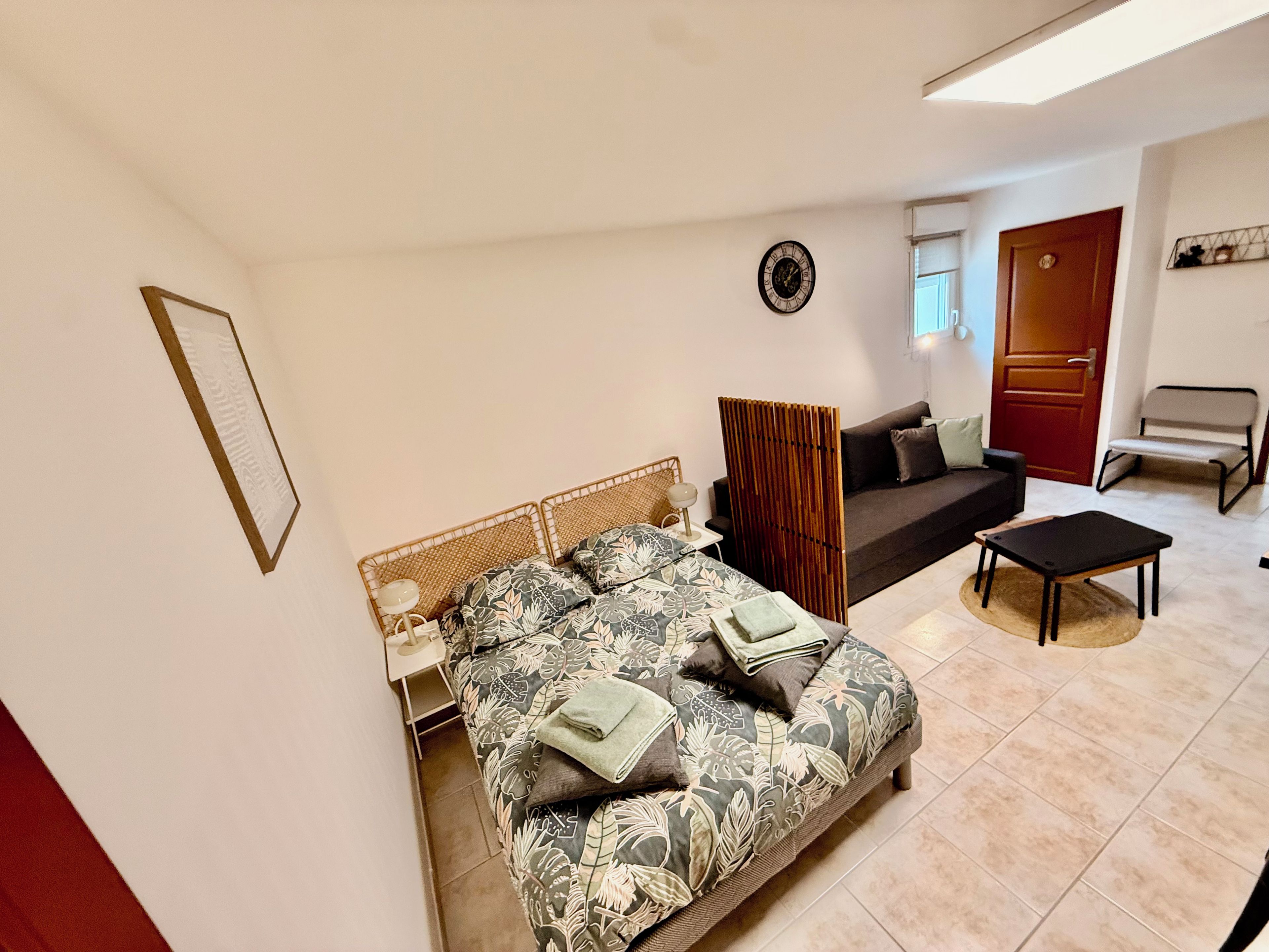 A bedroom with a bed, a bedside table, a chair, a sofa, and a door.