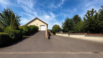 A paved driveway leading to a building with a garage door, surrounded by greenery and a clear sky.