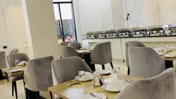 A dining area with tables and chairs, a buffet line, and a view through a large window.