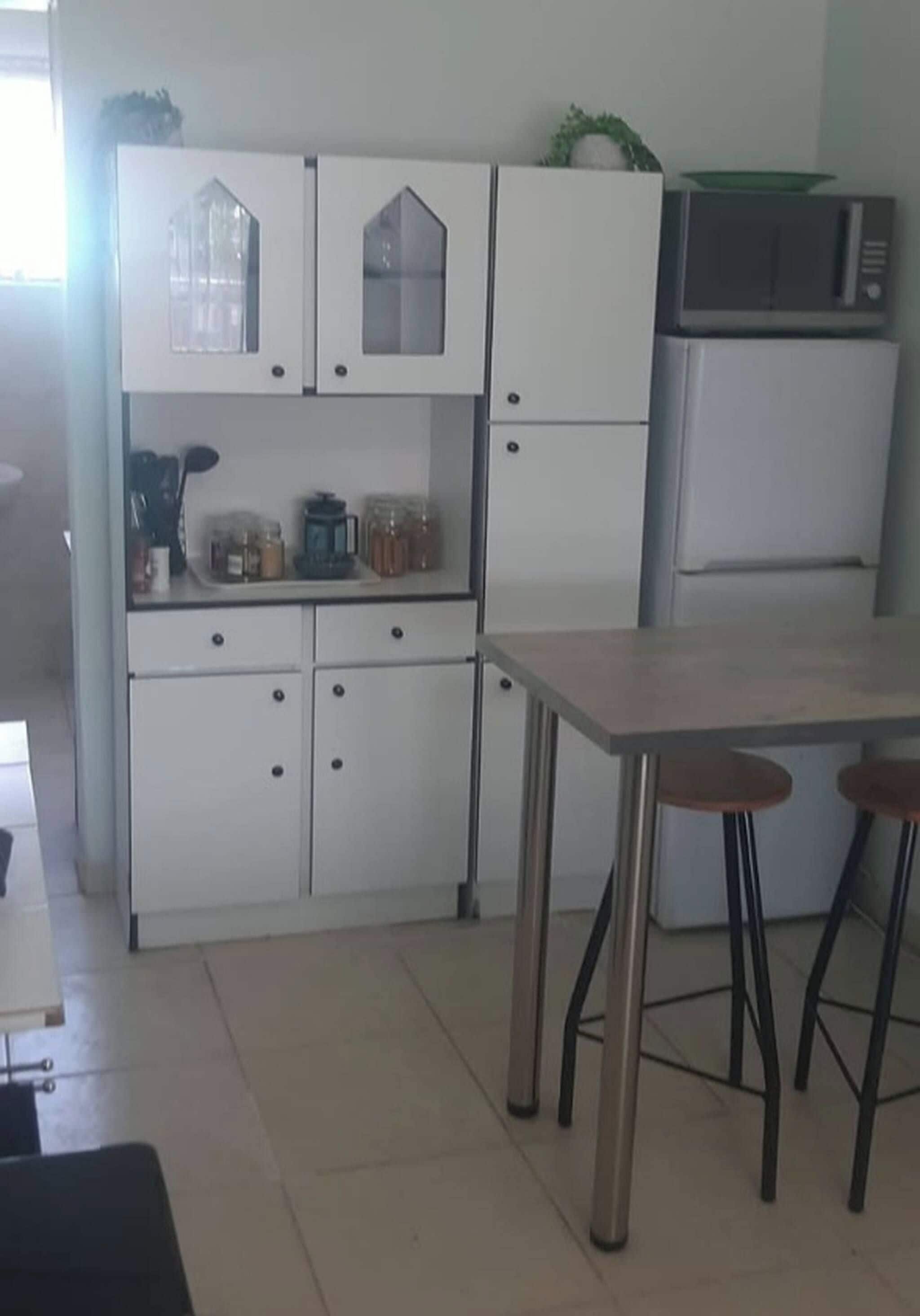 A kitchen with white cabinets, a refrigerator, a microwave, and a table with stools.